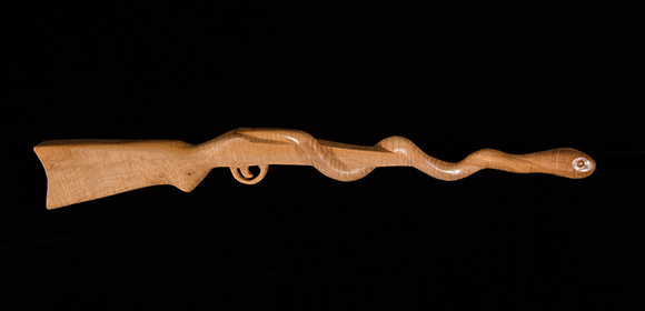 Photo of carved wood shotgun with snake wrapping around the basrrol on a black background.