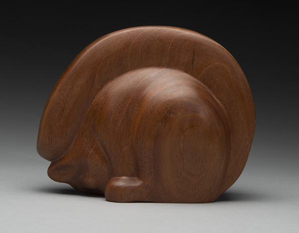 Wood carving of squirel sitting on a gray surface that is fading into black.