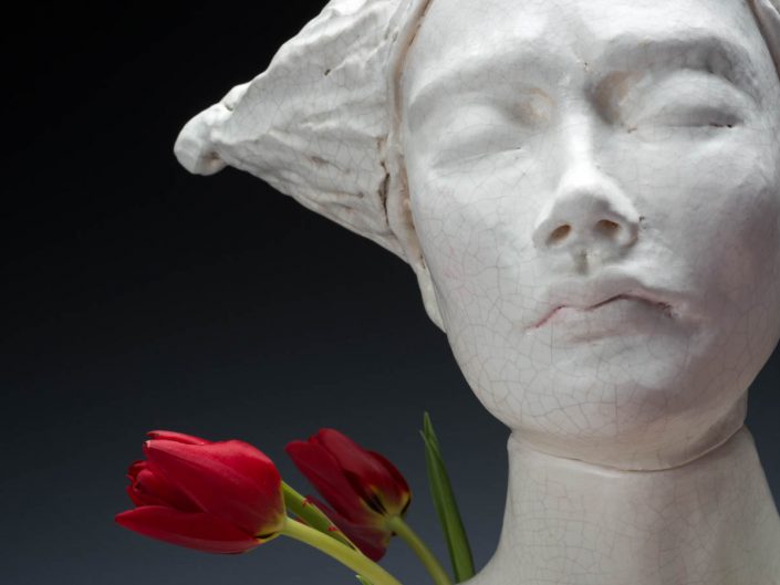 photograph of female bust sculpture with cracked white glaze and fresh flowers on black background
