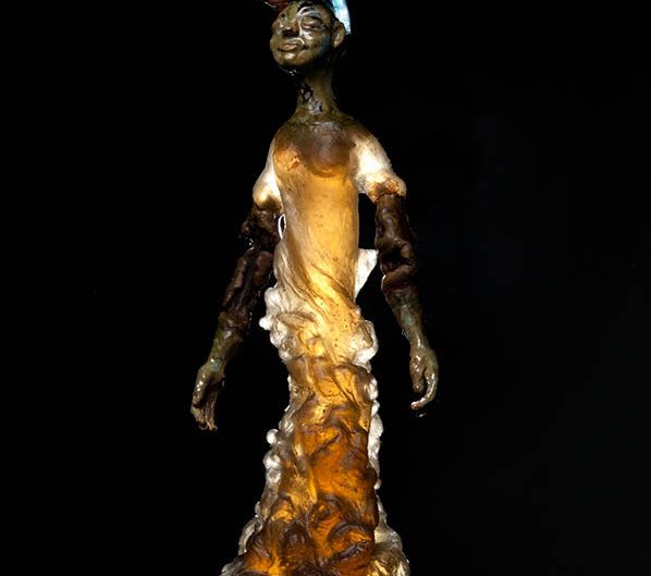 Photography of amber glass sculpture or woman standing with blue glass bird on head against a black background.